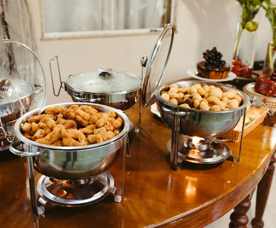 Stock photo: three round chafing dishes with glass lids on a wooden table, filled with golden fried bites and savoury pastries
